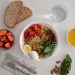A balanced meal featuring a variety of healthy ingredients including noodles, eggs, almonds, strawberries, and fresh vegetables.